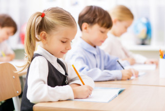 3 school children sat at their desks writing