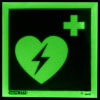 a front shot of the aed location sign glowing in the dark with a green heart with a lightening bolt through it with a first aid cross in the top right corner