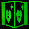 a full front shot of the panoramic aed wall sign with a green background, heart with lightening bolt through it and first aid cross in the top right corner glowing in the dark