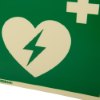 Close up of the panoramic aed wall sign showing a heart with a lightning bolt and a cross on green background