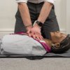 Hands performing compressions on laerdal little anne qcpr dark training manikin lying on the floor