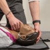 Person demonstrating head tilt on laerdal little anne qcpr dark training manikin lying on the floor
