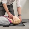 Person demonstrating head tilt on laerdal little anne qcpr light training manikin lying on a grey mat