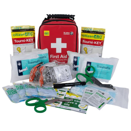 a red plastic carry case with a black handle with a white cross and the words first aid. In front is the contents of the trauma kit including blue gloves, tourni-keys, clothing shears and bandages 