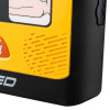Close‑up of a yellow AED showing part of the pad‑placement diagram, ventilation grooves, and the edge of an orange shock button.